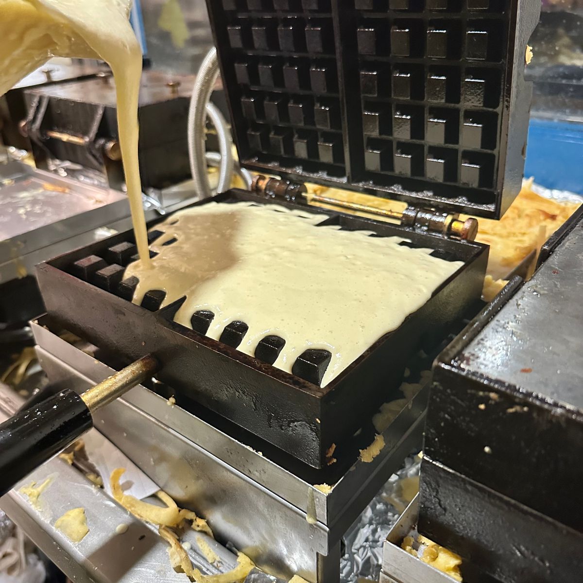 Het verse deeg voor onze Brusselse wafels dat in het toestel gegoten wordt, klaar om gebakken te worden tot heerlijke Brusselse wafels